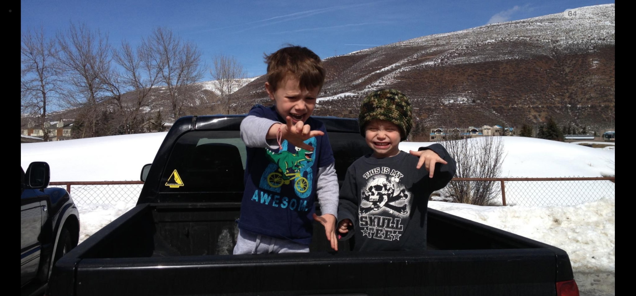Two children playing in the bed of a pickup truck with snow-covered hills behind them