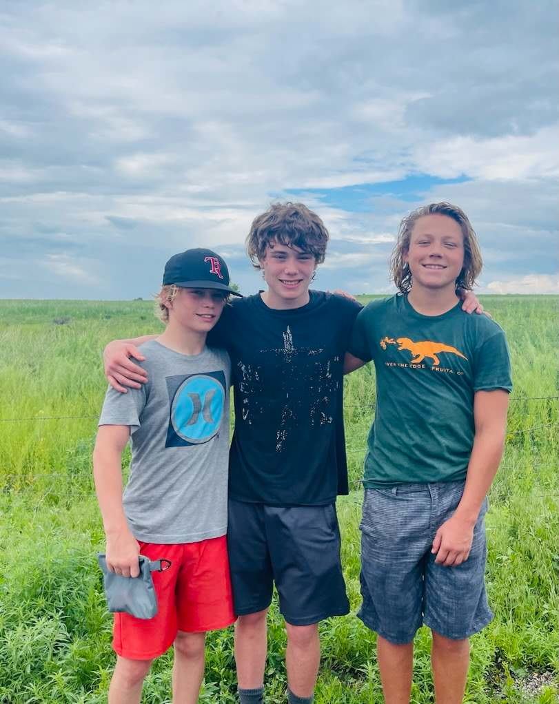 Three young people standing together in a green field