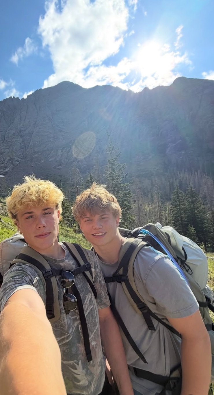 Cole and a companion with backpacks beneath a mountain ridge