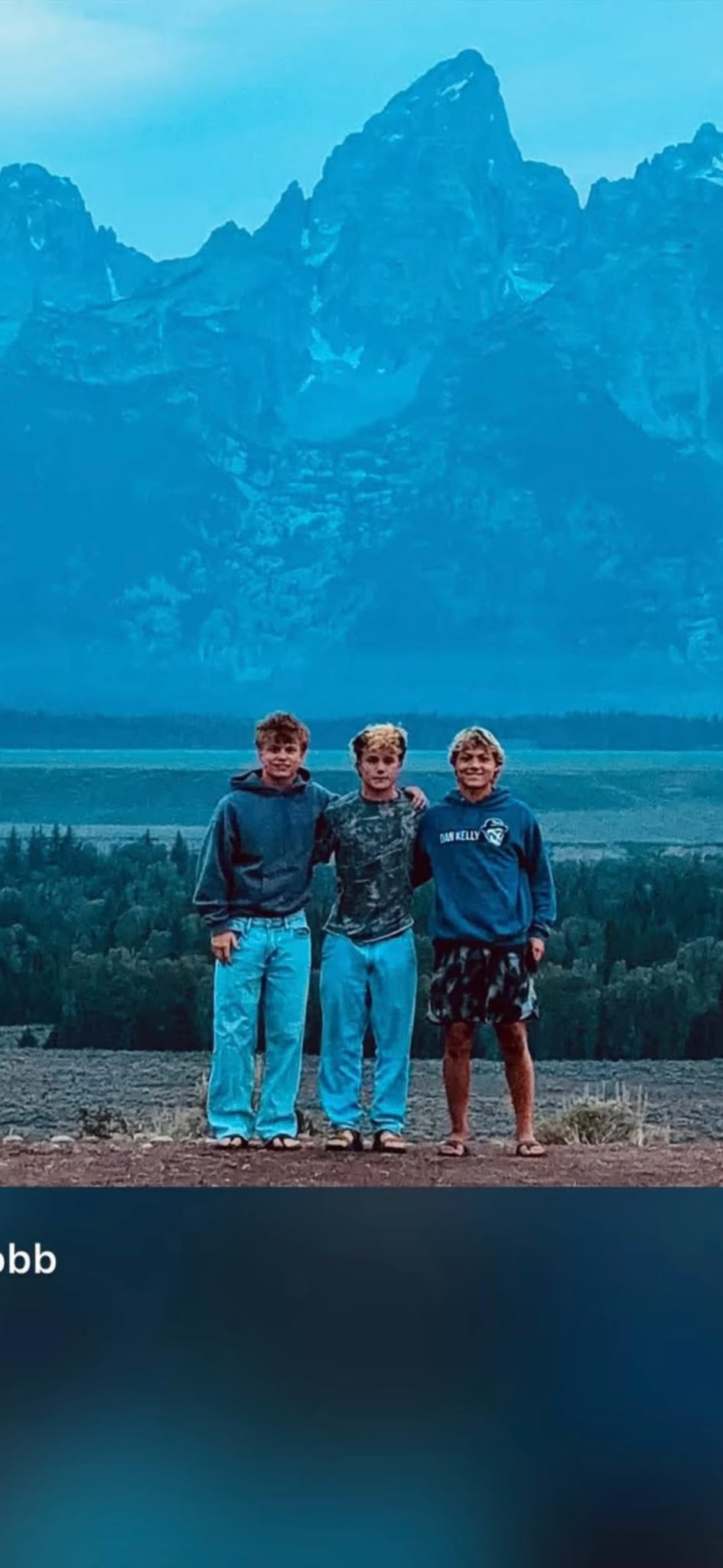 Three young people standing together beneath a mountain range
