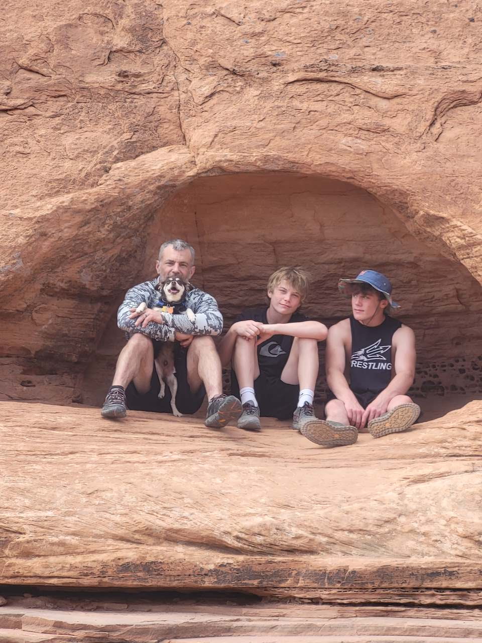 Three people and a dog resting in a red rock alcove