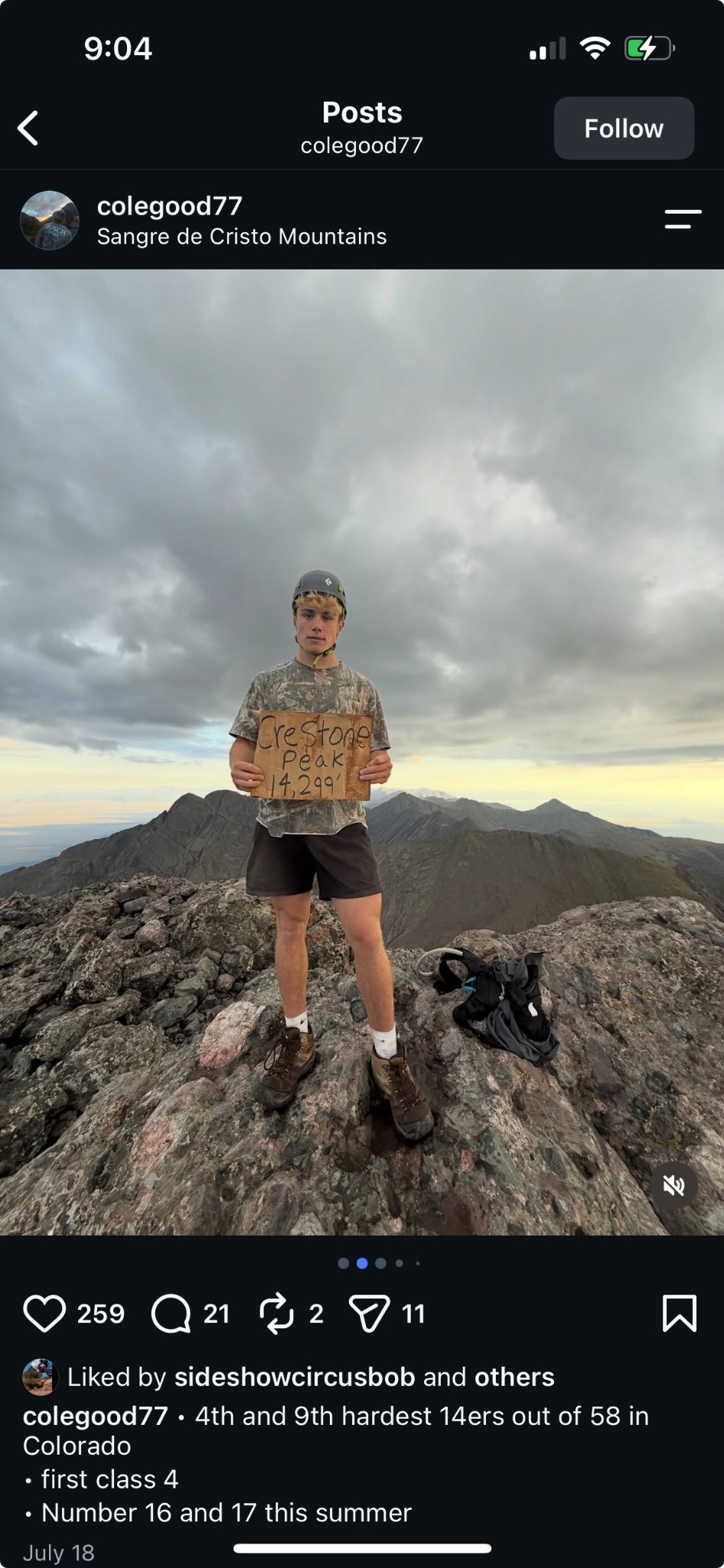Cole standing on a rocky summit holding a Crestone Peak sign