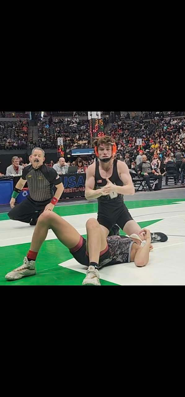 Teenage wrestlers competing on a mat with a referee nearby