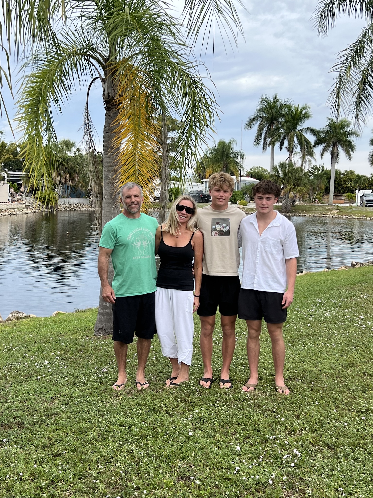 Four people standing together beside a pond and palm trees