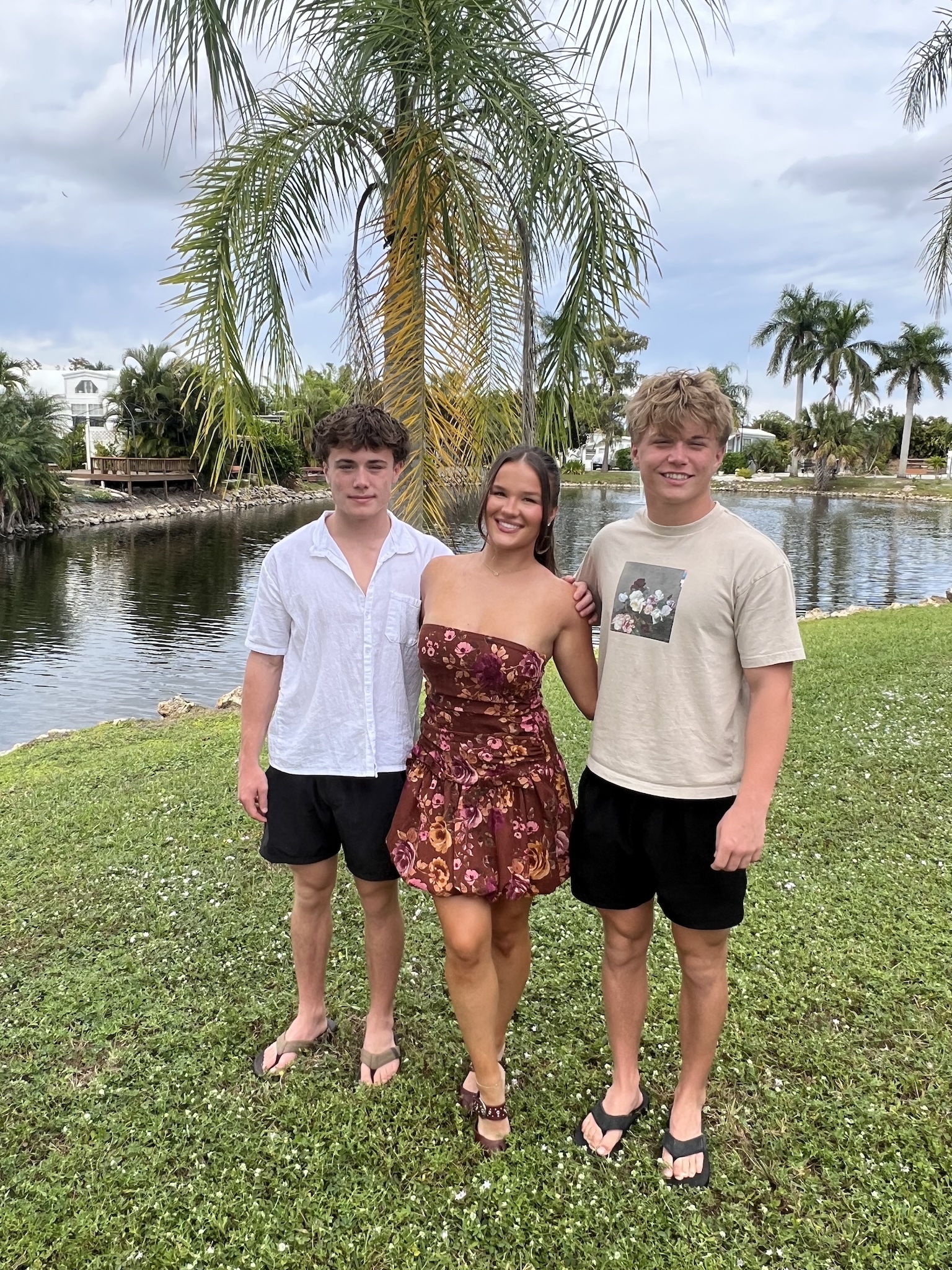 Three young people standing together beside a pond and palm trees