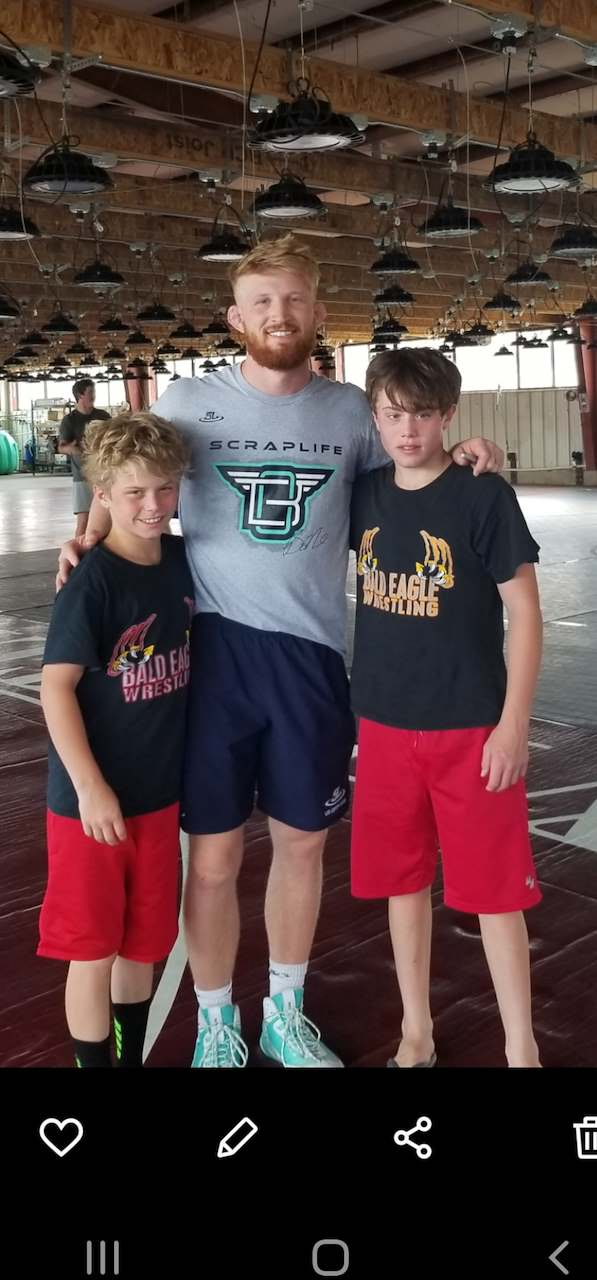Two young people in wrestling shirts standing with an adult in a training hall